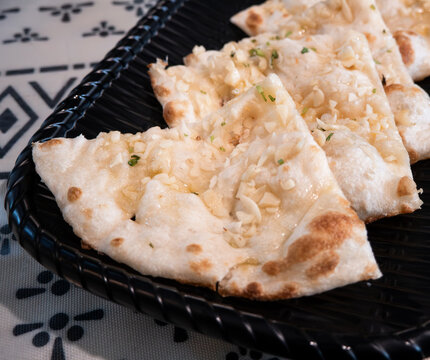 Fresh baked Indian naan flatbread slices served on a woven plate.