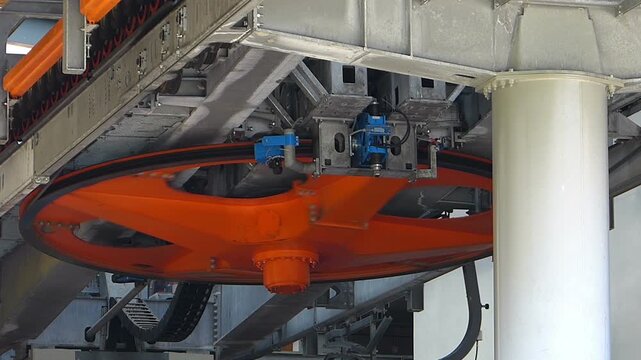 Close up shot of a giant bullwheel rotating a mountain ski lift cable with original audio. Industrial machinery mechanism of a chairlift transport system under bright sunshine in Bulgaria.