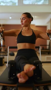 A fit woman is actively performing Pilates exercises on a reformer machine. She demonstrates controlled movements for strength and flexibility in a modern studio.