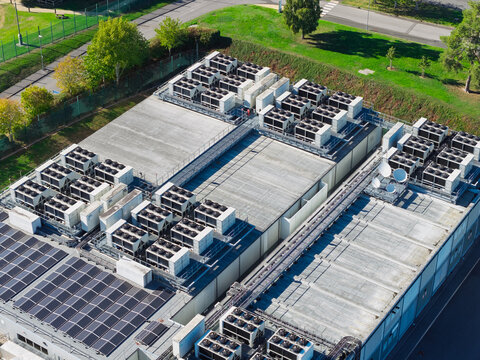 Aerial view of a data center roof featuring numerous HVAC cooling units, rows of solar panels, and satellite dishes, set within a fenced industrial perimeter in the United Kingdom.