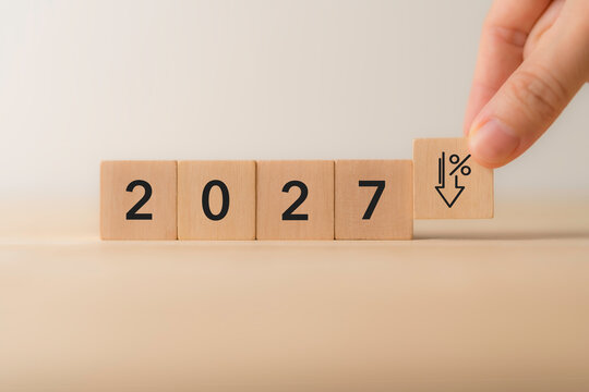 2027 Interest Rate Cuts. Declining Rates. Economic Outlook. Placing wooden block with a downward percentage arrow beside 2027. Interest rate cuts, declining rates, monetary policy, economic forecasts.