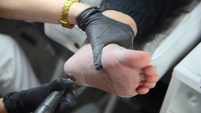 Hardware pedicure smoothing dry heel zone helps soothe painful cracked heels. Beautician wearing protective black gloves uses specialized milling cutter to gently exfoliate dead skin.
