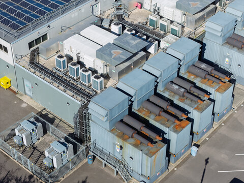Aerial view of a data center facility with industrial cooling units, HVAC systems, and solar panels on the roof, plus electrical transformers in a fenced enclosure in the United Kingdom.