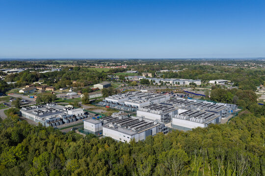 Aerial view of a data center facility surrounded by lush green trees and open landscape, United Kingdom.