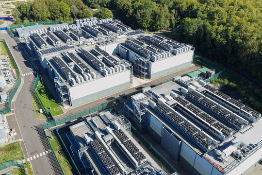 Aerial view of a large data center facility featuring multiple server buildings with extensive rooftop cooling units and surrounding trees in the United Kingdom.