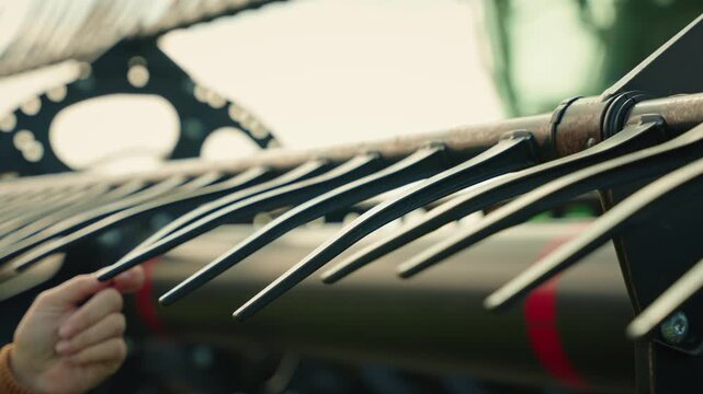 Static close-up of plastic tines on a combine header as a farmer moves down the row by hand, checking each component before reaching and inspecting the tine in focus