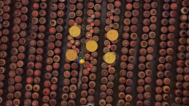 Vietnamese worker carrying buckets through rows of soy sauce jars