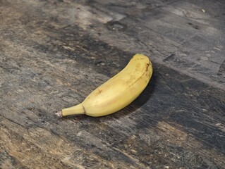 Ripe yellow banana with brown spots on dark textured wooden surface, overhead © Waldemar