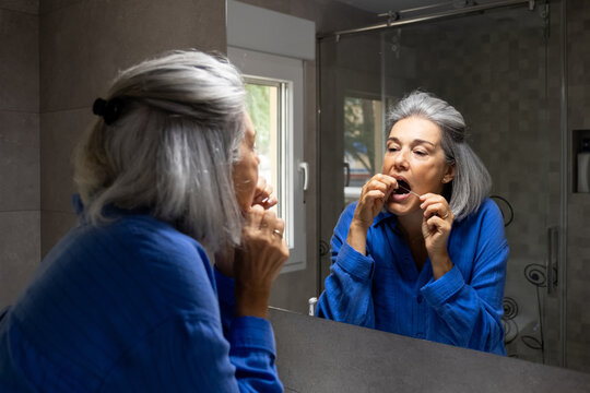 Woman flosses her teeth in the bathroom mirror in the morning
