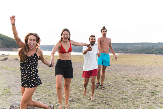 Cheerful male and female friends holding hands while walking at lakeshore