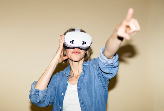 Woman wears virtual reality headset and points forward indoors