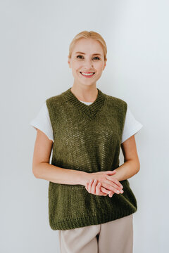 A smiling woman wears a green knit sweater vest indoors
