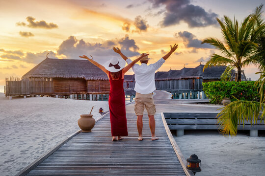 A happy couple enjoys a golden sunset on a wooden pier in the Maldives islands during their tropical vacation time