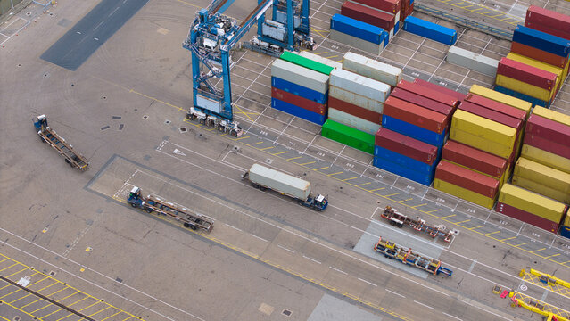 Aerial view of Port of Felixstowe showing colorful stacked shipping containers, a large gantry crane, and trucks maneuvering through industrial docks in Felixstowe, England, United Kingdom.