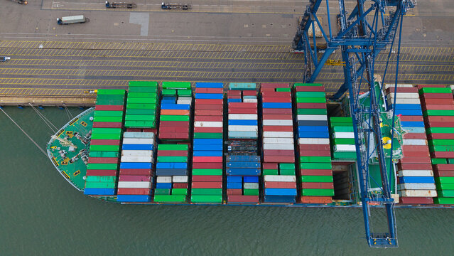 Aerial view of a large container ship docked at the Port of Felixstowe, featuring rows of colorful shipping containers and a massive loading crane in Felixstowe, England, United Kingdom.