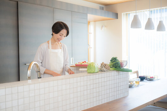 A Japanese housewife cooking with fresh vegetables in the stylish, open-concept kitchen of her home, bathed in bright backlight streaming through the window; an image of a lifestyle centered on home c