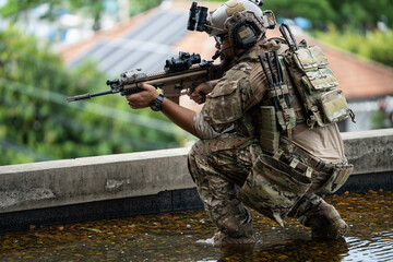 Fototapeta premium Male soldier in uniform and tactical helmet holding assault rifle while crouching on rooftop in urban area, military operation and tactical combat readiness
