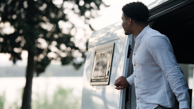 Man stepping out of a camper van, enjoying the scenic view during a relaxing road trip, embracing travel and adventure