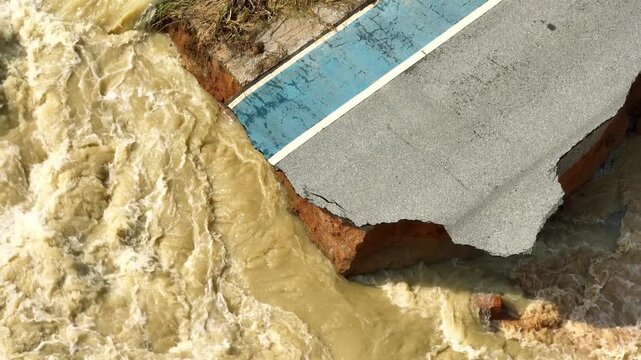 Drone photography documents a road washed away by powerful flood currents, exposing unstable soil layers and broken pavement while illustrating the consequences of extreme weather disasters. 4k.
