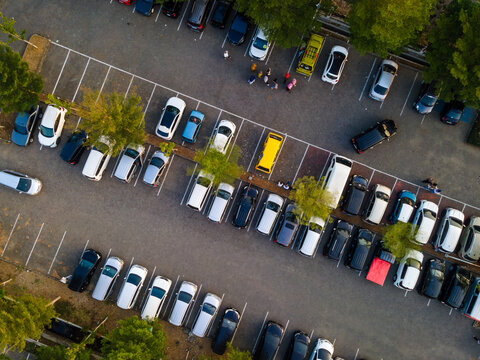 Aerial view of a parking lot filled with various cars, interspersed with green trees and small groups of people walking between vehicles in Purwokerto, Central Java, Indonesia.