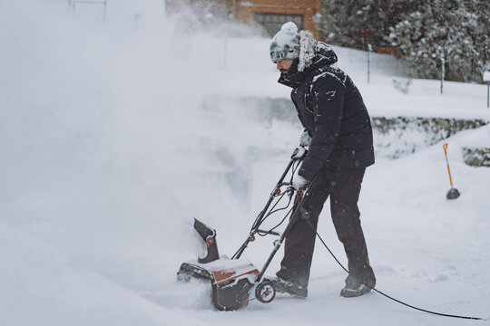 man clearing snowdrifts in countryside using electric snow blower on snowy winter day
