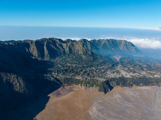 Majestic mountain range rises above vast valley. Clouds drift below rugged, sunlit peaks near Bromo © Cloudyew