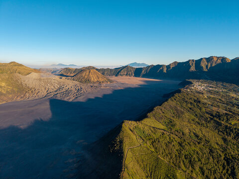 Sunlit mountains frame a vast, shadowed volcanic valley. Green slopes contrast with barren at Bromo