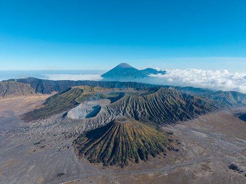 Aerial daytime panorama of Mount Bromo, its volcanic caldera, rugged ridges, ash plains, and distant cloud covered peaks.