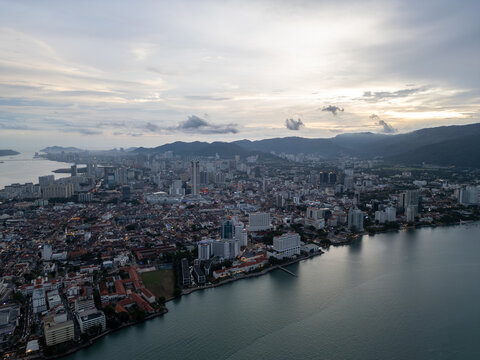 City sprawls along waterfront under soft, cloudy sky. Buildings stretch toward distant hills at George Town, Penang