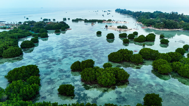 Aerial view of Pari island featuring lush mangrove forests in shallow turquoise waters, small sandy beaches, and calm sea in South Kepulauan Seribu, Jakarta, Indonesia.