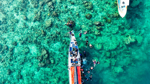Aerial view of people snorkeling and swimming around a boat in the clear turquoise waters of the coral reefs near Pari Island in South Kepulauan Seribu, Jakarta, Indonesia.