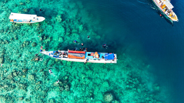 Aerial view of Pari Island with boats and people snorkeling in the clear turquoise waters of South Kepulauan Seribu, Jakarta, Indonesia.