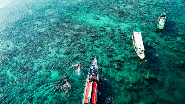 Aerial view of Pari island with boats and people swimming in the clear turquoise water over coral reefs in South Kepulauan Seribu, Jakarta, Indonesia.
