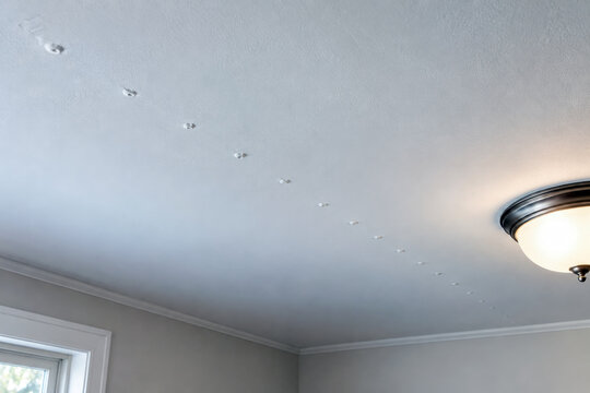 Row of nail pops along joist line on white ceiling beside light fixture - ceiling drywall repair and home inspection
