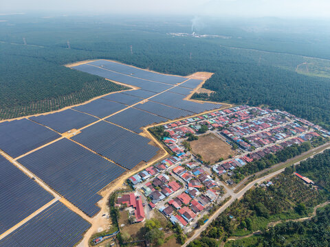 Aerial view shows solar panels across green fields. Village with red roofed homes nearby