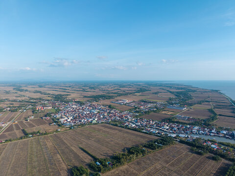 Aerial view of coastal village nestled between farmland and sea. Clear sky stretches above quiet at Tanjung Piandang, Perak