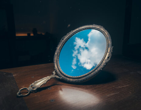 Vintage oval mirror reflection showing bright blue sky and clouds on dark background