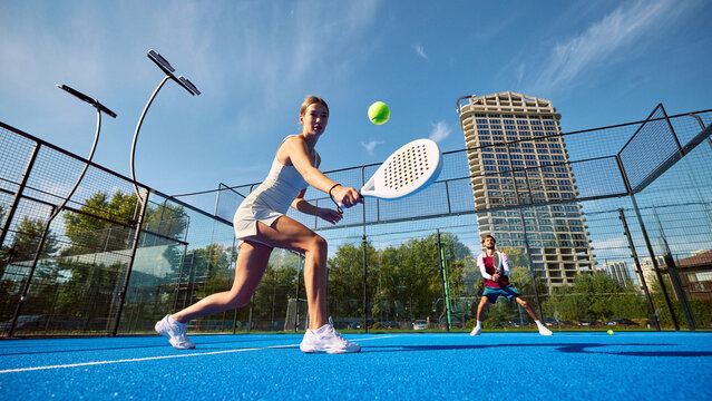 Forward padel stroke by female player with male partner ready on blue court. Women in sport, skill development concept.