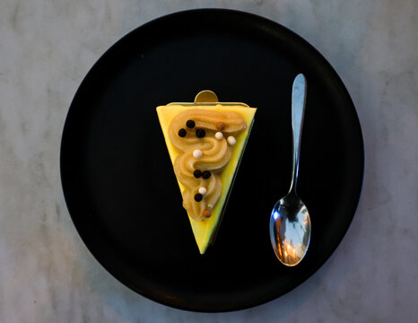 View of a slice of yellow cake topped with piped cream and chocolate pearls served on a black plate with a silver spoon in San Jose del Cabo, Baja California Sur, Mexico.