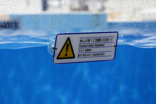 Close-up of a multilingual splash warning sign at an aquarium pool.