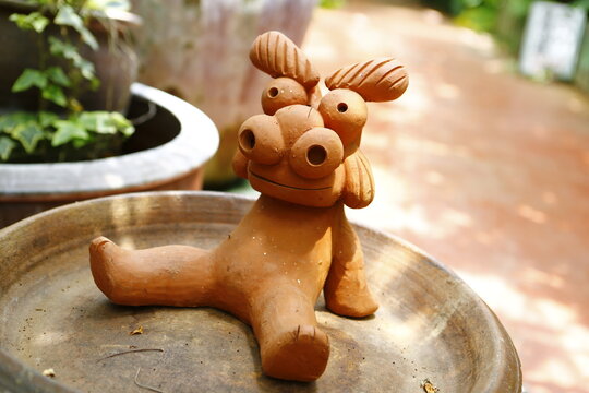A cute handmade Shisa pottery figurine relaxing in a garden.