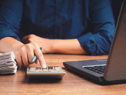 Person pressing calculator beside laptop and documents