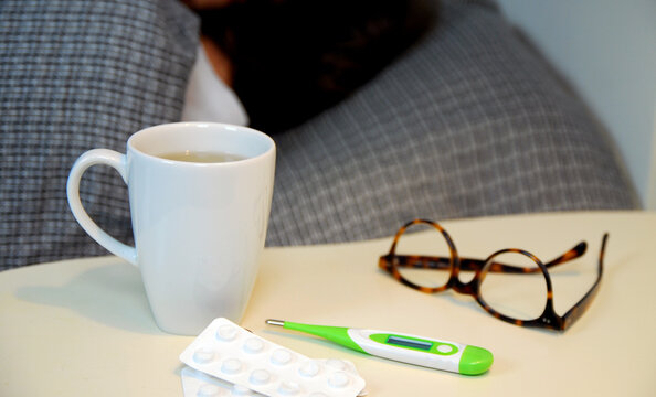 Erk&auml;ltungszeit: eine Person liegt krank im Bett, Nachttisch mit Tee, Fieberthermometer und Tabletten