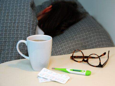 Erk&auml;ltungszeit: eine Person liegt krank im Bett, Nachttisch mit Tee, Fieberthermometer und Tabletten