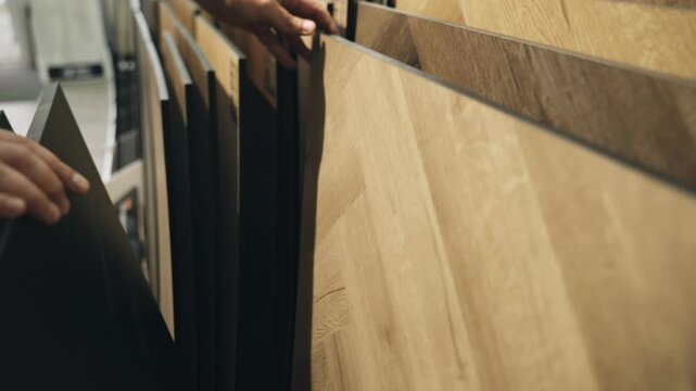 Showcasing a range of beautiful laminate and parquet materials, hands gently examine different styles and textures, perfect for enhancing any living space with elegance and warmth.