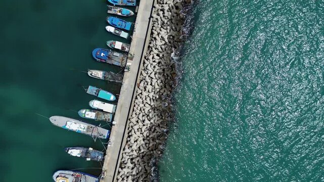 Aerial View of Fishing Boats Moored at Breakwater Pier in Blue Sea Water