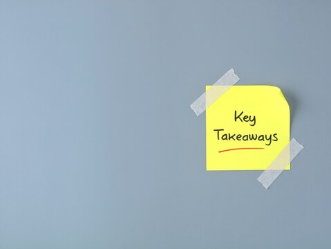 Key takeaways text handwritten on yellow adhesive note taped on a grey background with copy space, ideal for business concept, meeting summary, education, and presentation background