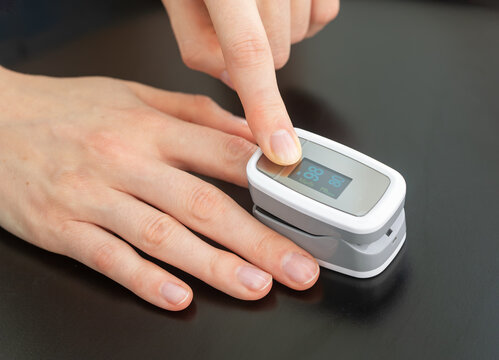 Index finger presses button on a pulse oximeter, reading oxygen saturation and SpO2. Fingertip sensor tracks heart rate and blood oxygen. Close up, home checkup gadget.