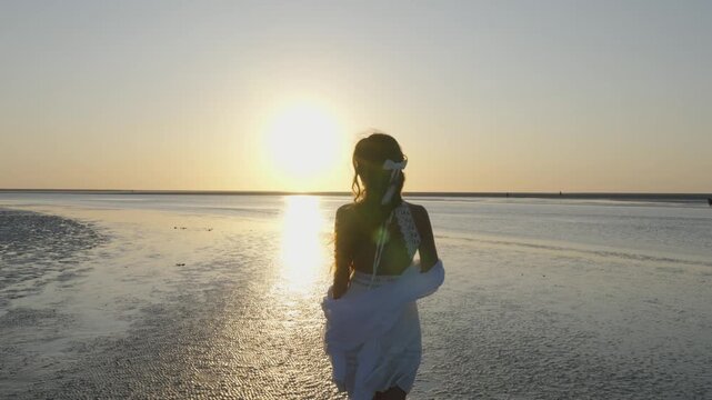 Woman in white dress facing low sun on Mont Saint Michel tidal flats