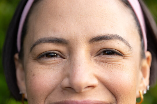 Adult woman smiling with eyes squinting, wearing pink headband, hoop earring and studs outdoors
